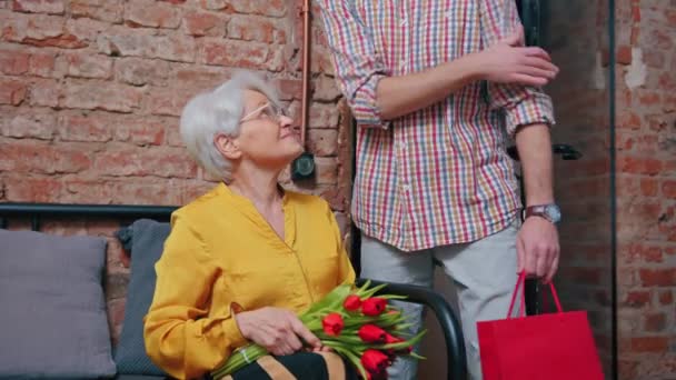 Ηλικιωμένη Ευρωπαία γυναίκα που ξαφνιάζεται ευχάριστα από τον μεσήλικα γιο της που της δίνει λουλούδια και ένα δώρο — Αρχείο Βίντεο