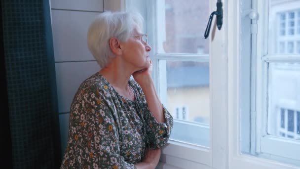 Пожилая женщина пенсионерка смотрит в окно, сидя в своем доме — стоковое видео