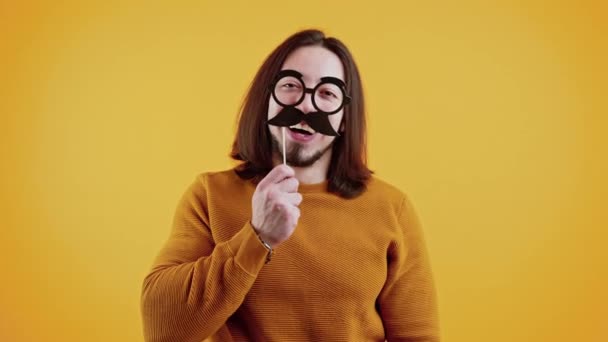 Divertido concepto de disfraz. Hombre caucásico adulto con gafas falsas y bigote sobre fondo amarillo. — Vídeos de Stock