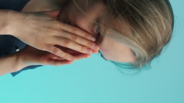 Verticale video Uitgeputte blanke verpleegkundige medisch verzorger in de 30 bedekte haar gezicht met twee handpalmen over een blauwe achtergrond. Studioshoot. — Stockvideo