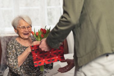 Yaşlı, gri saçlı, emekli bir kadının orta yaşlı oğlu Anneler Günü 'nden bir buket ve hediye almasına hoş bir sürpriz oldu. 