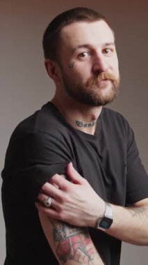 Ciddi sakallı, çekici genç bir Avrupalı adam dövmeli elini dikey video gradyan arka plan çekimine gösteriyor. 