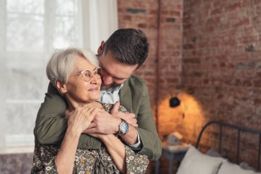 hug between caucasian elderly mother and her middle-aged bearded son medium shot