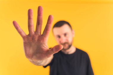 young bearded attractive European man extanding an opened hand towards the camera medium closeup orange background studio shot 