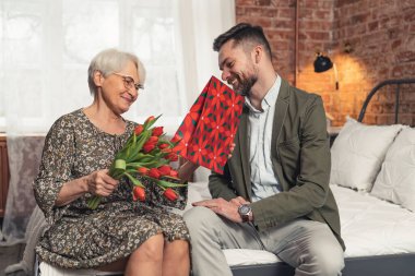 Büyükanne orta yaşlı torunuyla yatakta oturuyor ve ona verdiği güzel hediyelere bakıyor.