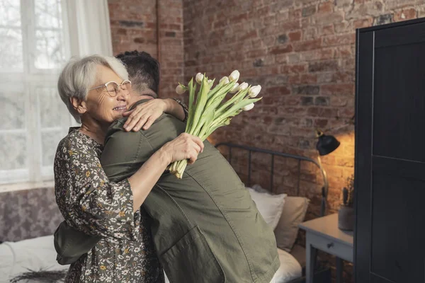 Äldre kaukasiska kvinna med glasögon får en kram av sin medelålders kaukasiska son — Stockfoto