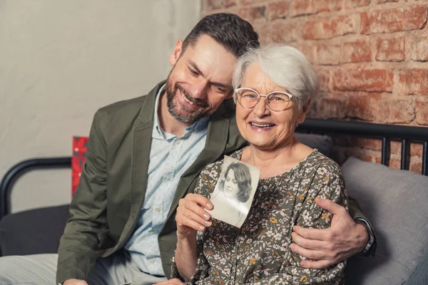 European relatives with age difference hugging and celebrating Mothers Day, elderly mother holding a picture of her younger self — Stockfoto