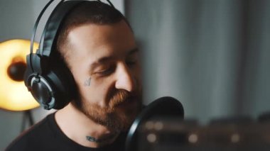 Stüdyoda kulaklığı ve mikrofonu olan yakışıklı, Avrupalı dövmeli bir adam stüdyoda orta ölçekli bir çekim odası arkaplanı kaydediyor.