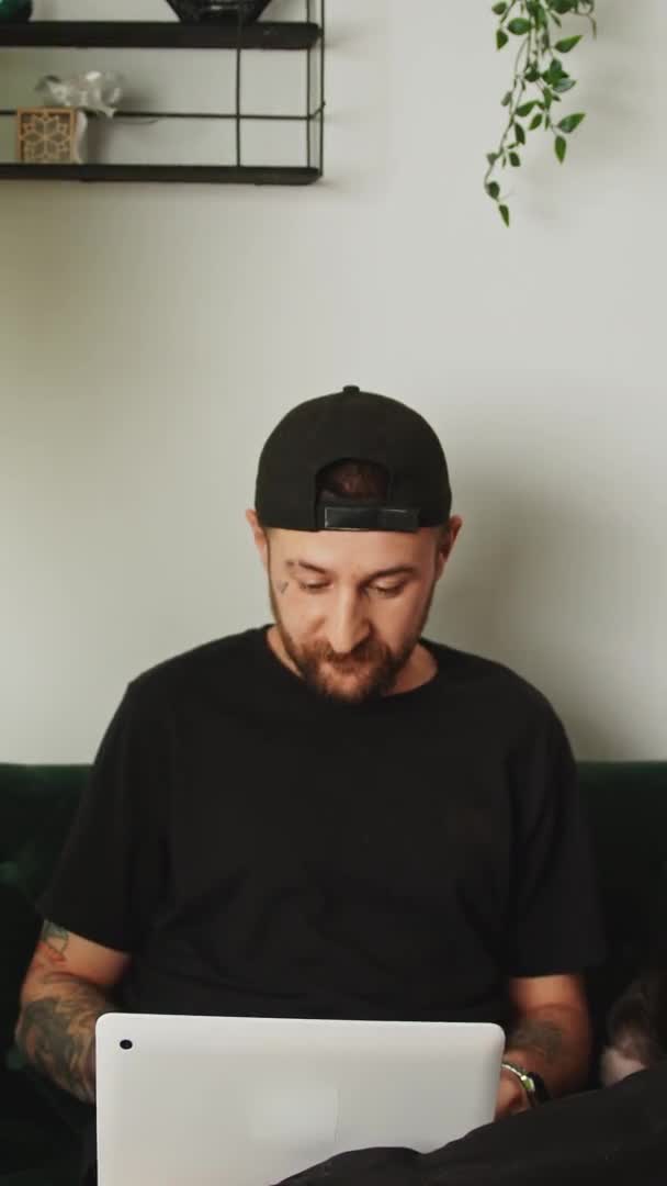 Вертикальне відео бородатий молодий чоловік з шапочкою татуювання, що працює на фріланс-концепції домашнього фону ноутбука — стокове відео