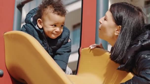 Mørkhåret kvinde og sød lille dreng med sort krøllet hår ser hinanden og kysse medium skudt udendørs – Stock-video
