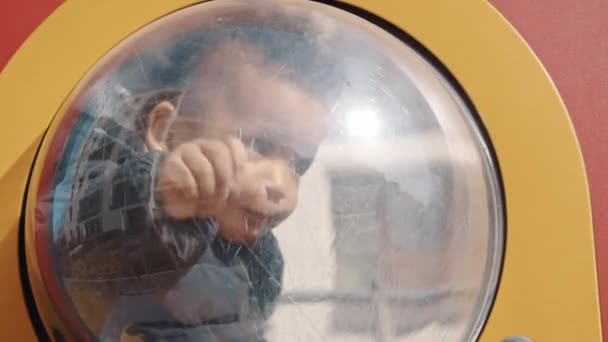 Parktaki plastik evde oturan küçük çocuk dışarıdaki cam bir medyuma dokunuyor. Pembe ve turuncu arka plan. — Stok video