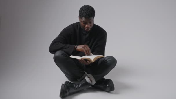 Melancholic pensive black man sitting with a book - fullshot — стоковое видео