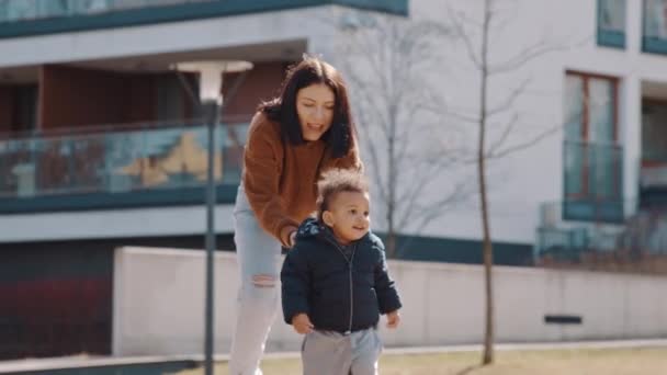 Happy and excited african-american little curled boy running from his mother in the park medium full shot outside urban background — Wideo stockowe