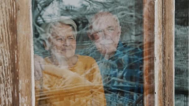 Old Caucasian married couple watch through the window and look at each other copy space middle shot — Vídeo de Stock