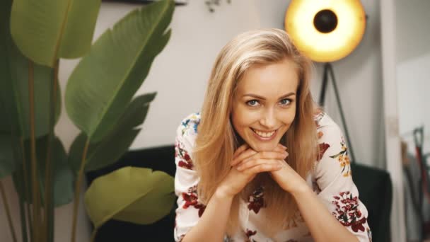 Portret van een jonge flirterige blonde vrouw op zoek naar de camera in een modern appartement — Stockvideo