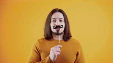 Sahte kağıt bıyık tarafından yaratılmış beyaz sakallı bir adamın stüdyo portresi. Ilık sarı arka planda izole edilmiş stüdyo çekimi.