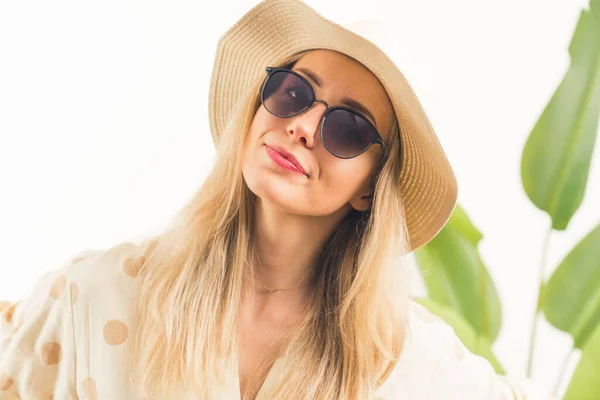 Lovely Caucasian blonde girl with black sunglasses and hat looking into the camera white background with green leaves medium closeup studio shot copy space — Stock Photo, Image