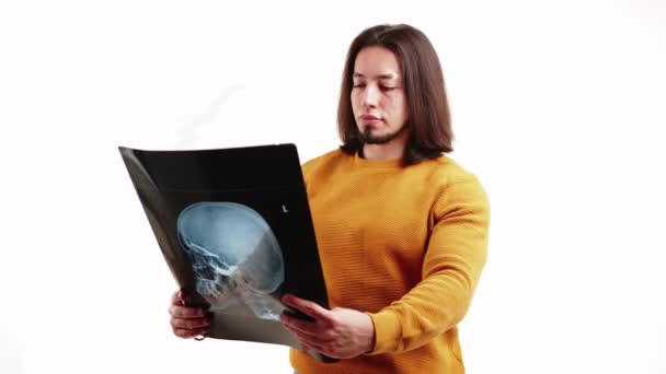 Uomo barbuto caucasico che tiene la radiografia del cranio mentre indossa una felpa gialla. isolato su sfondo bianco. — Video Stock