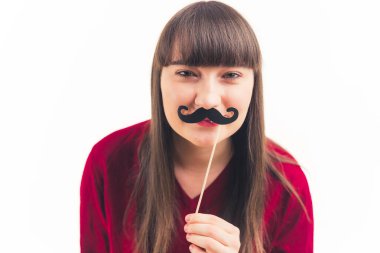 Çekici Kafkasyalı genç kadın kameraya bakar ve yüzünün önünde sahte bıyık tutar. Beyaz arka plan fotokopi stüdyosu çekilir. 