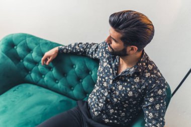 Kanepede oturan ciddi Latin Amerikalı adam orta boy arka plan çekim stüdyosunun yanı sıra yukarıdan çekilmiş.