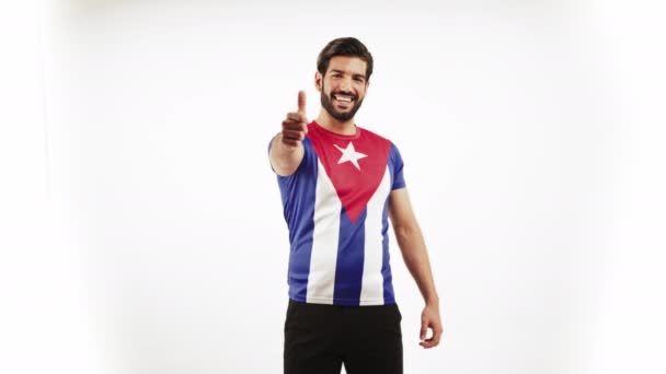 Young handsome Latin man standing satisfied because of his Cuban flag T-shirt and pointing to it infinity white medium shot studio shot country Cuban concept copy space — Vídeos de Stock