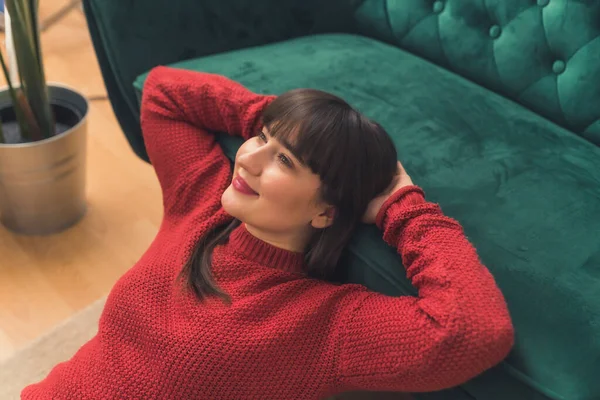 Smiling young Caucasian woman laying on the floor, leaning on the sofa, keeping her hands behind her head medium closeup copy space — 스톡 사진