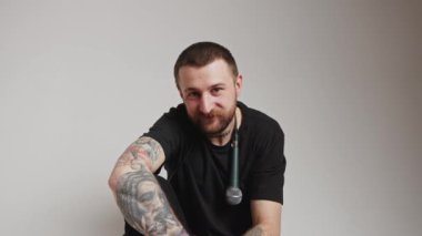 Gülümseyen sakallı, mikrofonlu yakışıklı genç Avrupalı adam kameranın gradyan gri arka plan görüntüsüne bakıyor. 