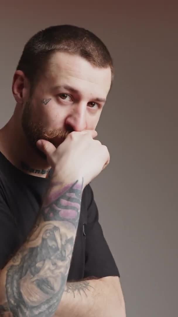 A serious tattooed European man standing and thinking vertical video studio shot medium closeup gradient background — Stock video