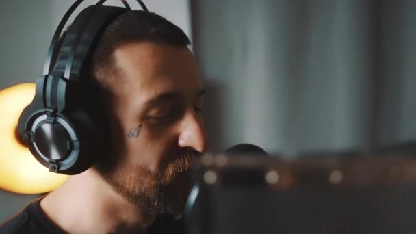 Caucasian attractive man with headphones singing in a microphone in studio closeup indoor studio shot room background — Vídeo de stock