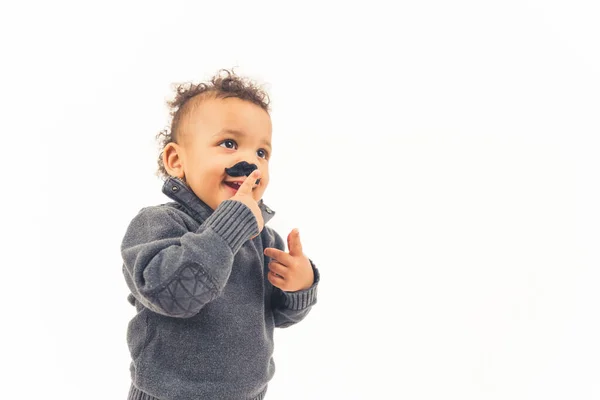 Funny happy hipster biracial kid touching his fake black mustache props over white background. — Photo