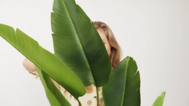 Çekici Avrupalı mavi gözlü güzel gülüşlü sarışın kız yeşil yaprakların arkasında duruyor.