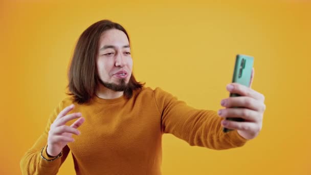 Homme caucasien barbu excité parlant sur un chat vidéo smartphone. Studio tourné sur fond jaune. — Video