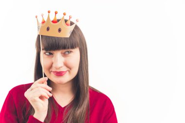 Ortalama yakın plan güzel bin yıllık kadın kafasının üstünde kağıt taç tutuyor, izole edilmiş stüdyoya bakıyor beyaz arka plan fotokopi alanı. 