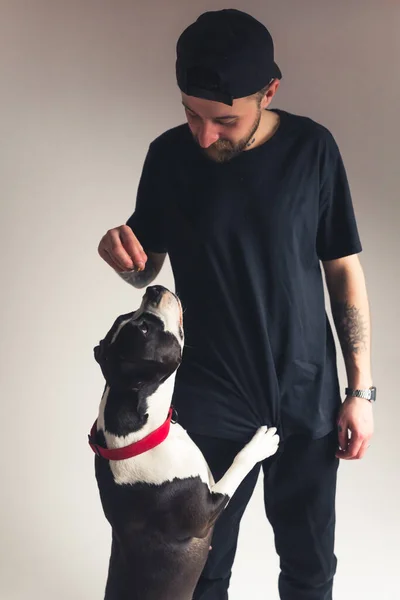 Vertical studio shot d'un propriétaire de chien gars en vêtements noirs donnant friandises pour chiens à son meilleur ami animal. — Photo