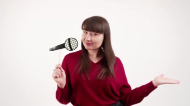 Young beautiful caucasian dark-haired woman singing with props fake microphone over white background.