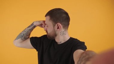 Kafkasyalı gangster dövmeli genç bir adamın stüdyo fotoğrafı. Pazılarını esnetiyor ve sarı arka plan üzerinde gözlerini dikiyor..
