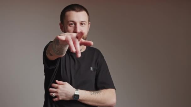 Evropský vousatý raper hudební tvůrce chlap s tetováním rukávy v černém tričku ukazuje na kameru a poskakuje s vážným výrazem obličeje. — Stock video