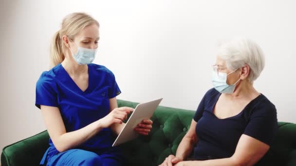 Monthly checkup routine. Elderly retired short-haired lady in a black t-shirt is being examined by a young caucasian blonde female healthcare professional worker. — Vídeo de Stock