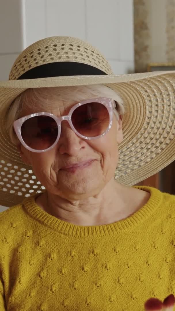 Vertical video of elderly woman smiking with modern sunglasses and wearing a hat, slowmo — Stock Video