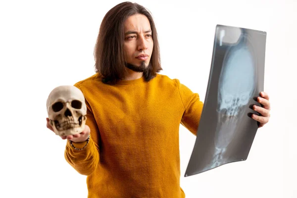 Frowned European man holds skull and x-ray, looks closely at the x-ray white background studio shot isolated — Stockfoto