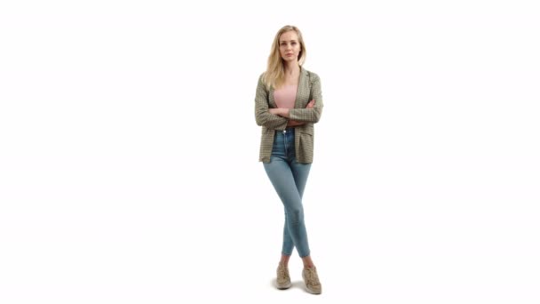 Ładny europejski blondynka dziewczyna stoi z ramionami skrzyżowane i patrząc krytycznie w aparat w trampki dżinsowe kurtka i różowa koszula studio strzał pełny strzał biały tło — Wideo stockowe