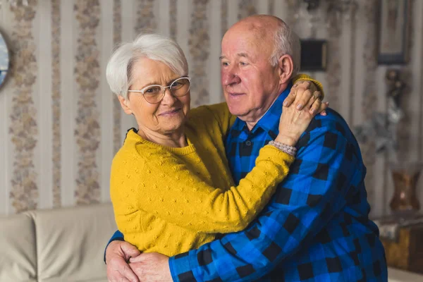 Content elderly caucasian heterosexual couple hugging in the living room. Happy retirement concept. — Stockfoto