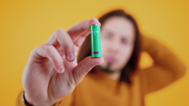 Battery held near to the camera. Focus on foreground. Caucasian man thinking about ecology and recycling over yellow background. Studio shot. — Vídeos de Stock