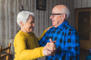 Ortak emeklilik kavramı. Yaşlı çift yıldönümlerini klasik oturma odalarında mutlu bir şekilde dans ederek kutluyor..