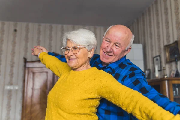 Elderly caucasian couple - grandmother and grandfather - dancing vividly in their old-fashioned apartment. Happy retirement concept. — Stockfoto