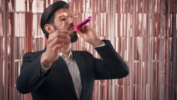 Latino bello giovane uomo indossa abito elegante che celebra tenendo il scintillante e fischio, sfondo rosa glamour — Video Stock