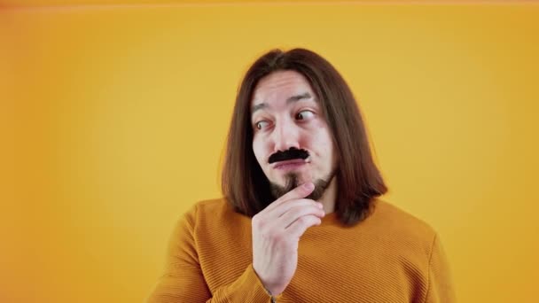 Movember. Alegre hombre caucásico de pelo largo con sudadera amarilla y bigote falso sobre fondo amarillo. — Vídeos de Stock