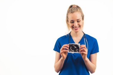 Beyaz, sarışın kadın doktor doğum öncesi ultrason taraması yapıyor ve gülümsüyor. Beyaz arka planda orta stüdyo çekimleri.