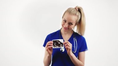 Neşeli, beyaz, sarışın kadın doktor doğum öncesi ultrason taraması yapıyor ve gülümsüyor. Beyaz arka planda orta stüdyo çekimleri.