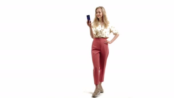 Beauté blonde confiante, jeune fille européenne prenant une vidéo pour ses adeptes des médias sociaux ou utilisant un appel vidéo pour communiquer avec ses amis et sa famille. Espace de copie, fond blanc. — Video